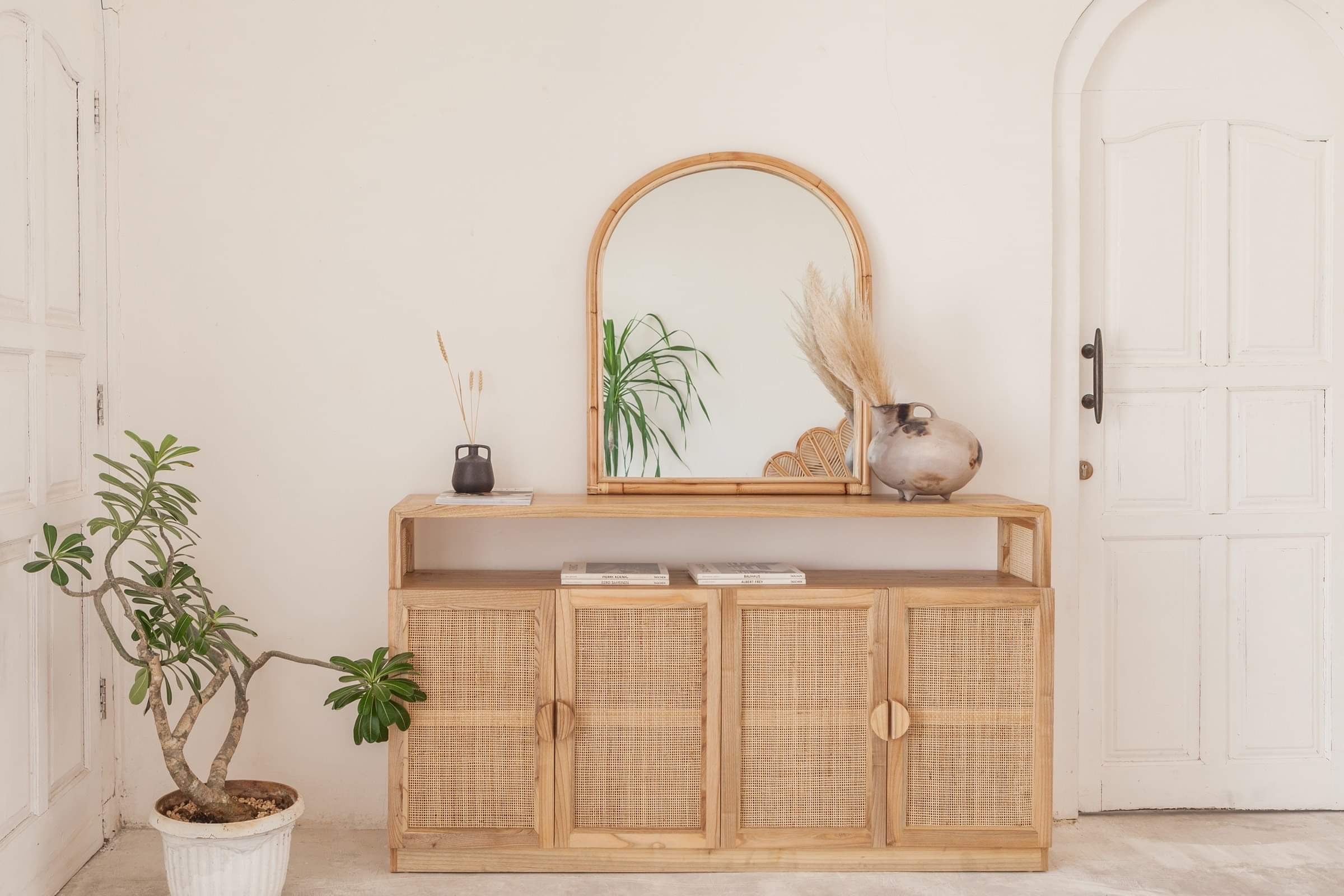 Asha Rattan Arched Mirror lent on top of the Dasha buffet, styled with plants and a rustic white door in the background.