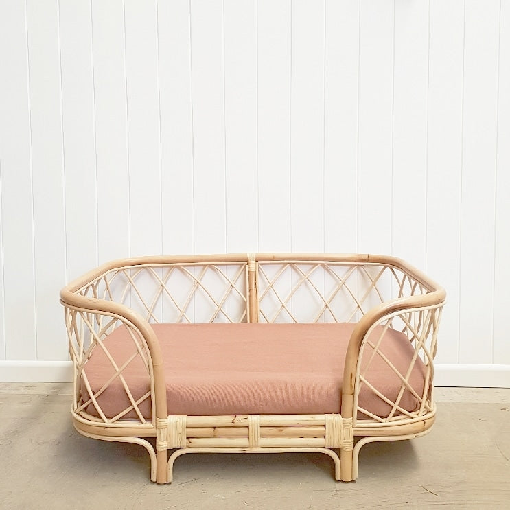 Bella rattan dog bed with clay coloured sheet positioned in front of a white wall. 