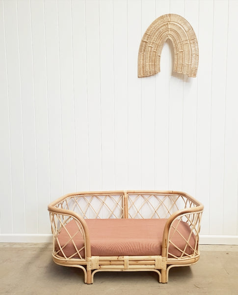Bella rattan dog bed with clay coloured sheet positioned in front of a white wall. 