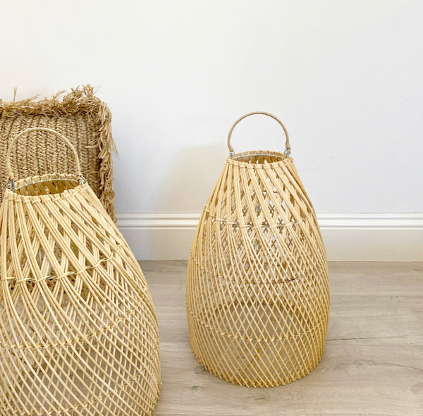 2 Ava rattan pendent light shades on the ground next to each other with a rattan cushion behind them.