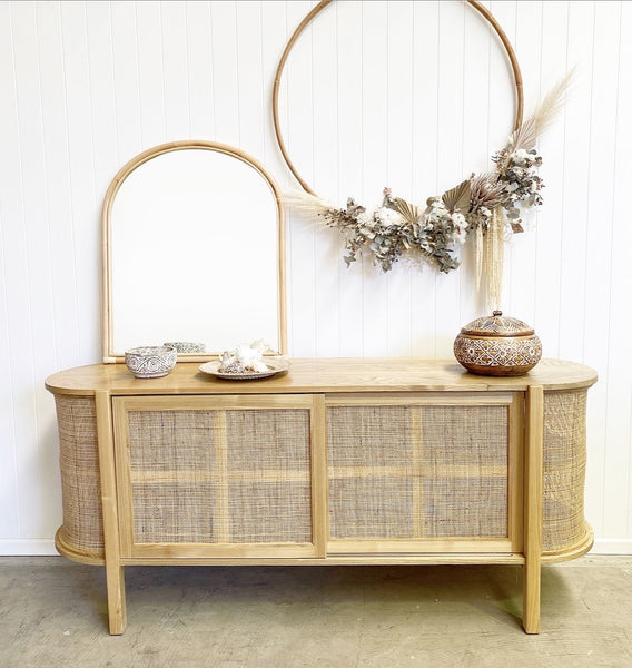 Asha Rattan Arched Mirror lent on top of the Florence Rattan Buffet and displayed with costal styling decor, reflecting a homewares shop with other rattan items.