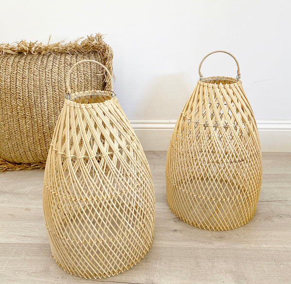 2 Ava rattan pendent light shades on the ground next to each other with a rattan cushion behind them.